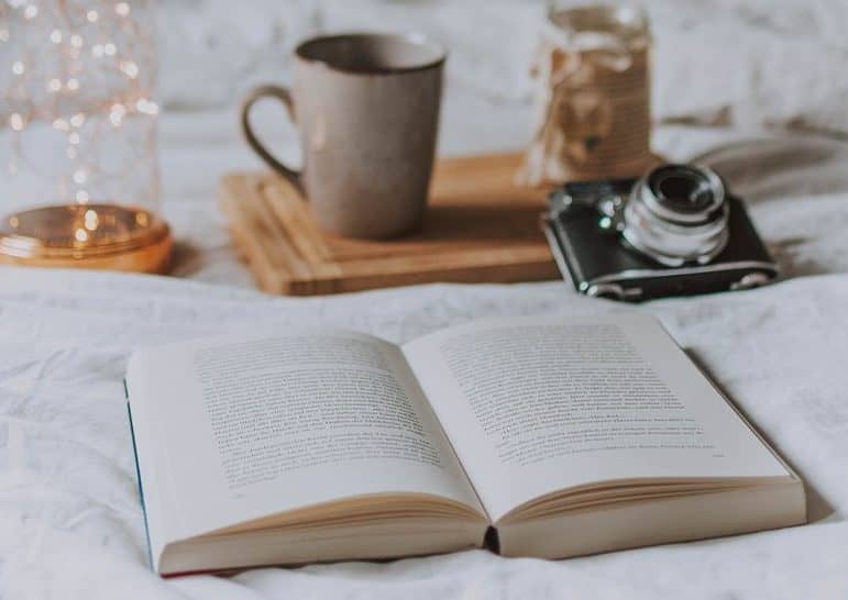 Fairy lights wound over a bed containing a serving board with tea mugs and an open book
