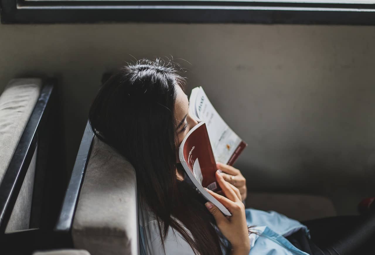 Woman has an open paperback book pressed against her face as though to breathe in the smell